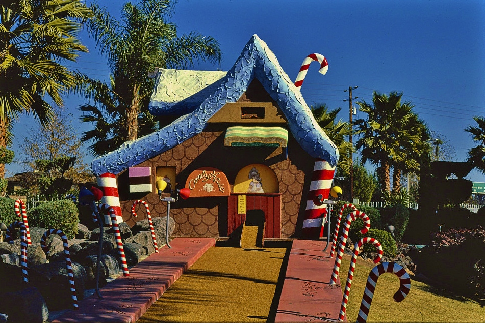 Colorful house made of candy at death's door at miniature golf course with palm trees and trimmed green bushes.